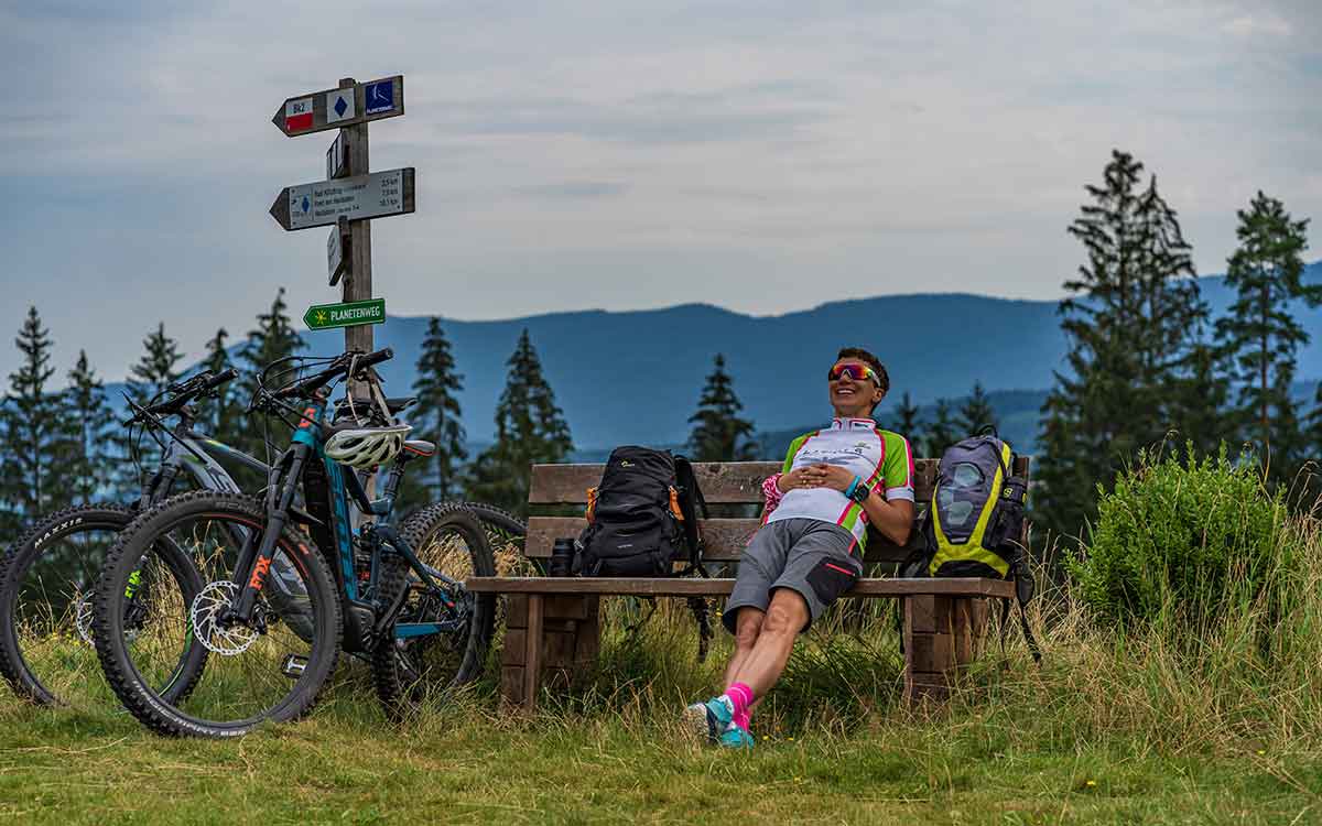 Radfahrer macht eine entspannte Pause auf einer Bank während einer Fahrradtour im Bayerischen Wald, in der Nähe des Wellnesshotels Waldeck.