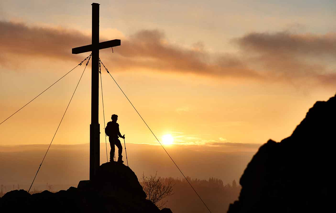 Bergsteiger erreicht das Gipfelkreuz nach einer Wanderung auf dem Silberberg im Bayerischen Wald, nahe dem Wellnesshotel Waldeck