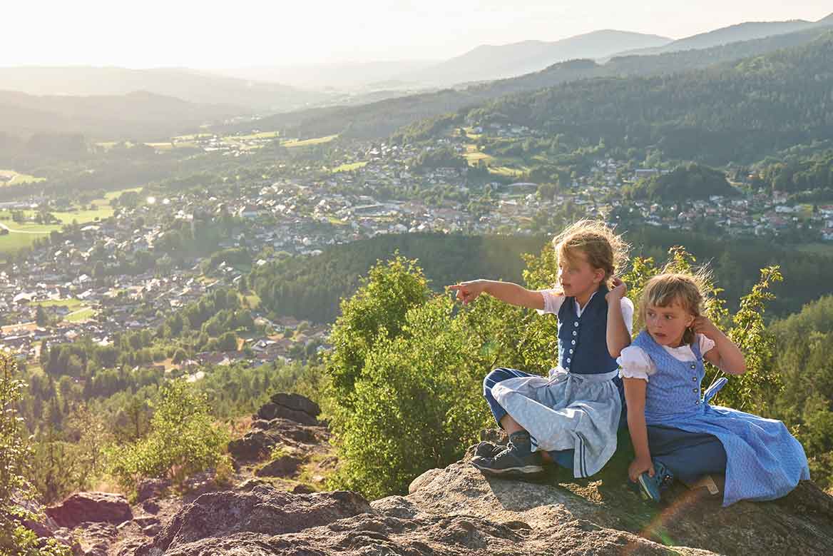 Zwei Kinder sitzen zusammen auf dem Silberberg und blicken ins Tal im Bayerischen Wald.