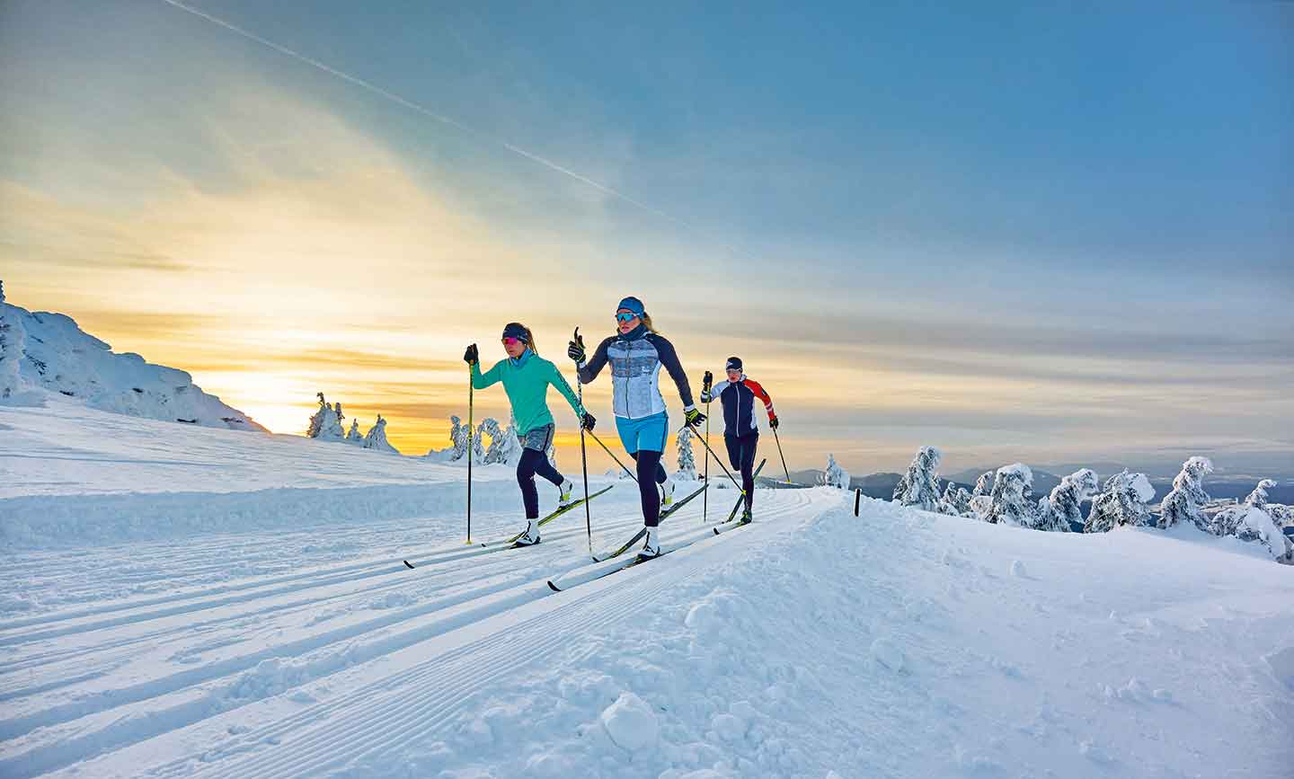 Langläufer auf einer verschneiten Loipe am Berg bei Sonnenaufgang im Bayerischen Wald.