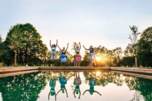 Vier Frauen im Dirndl springen fröhlich in den Biotop-Swimmingpool im Wellnesshotel Waldeck Bodenmais im Bayerischen Wald.