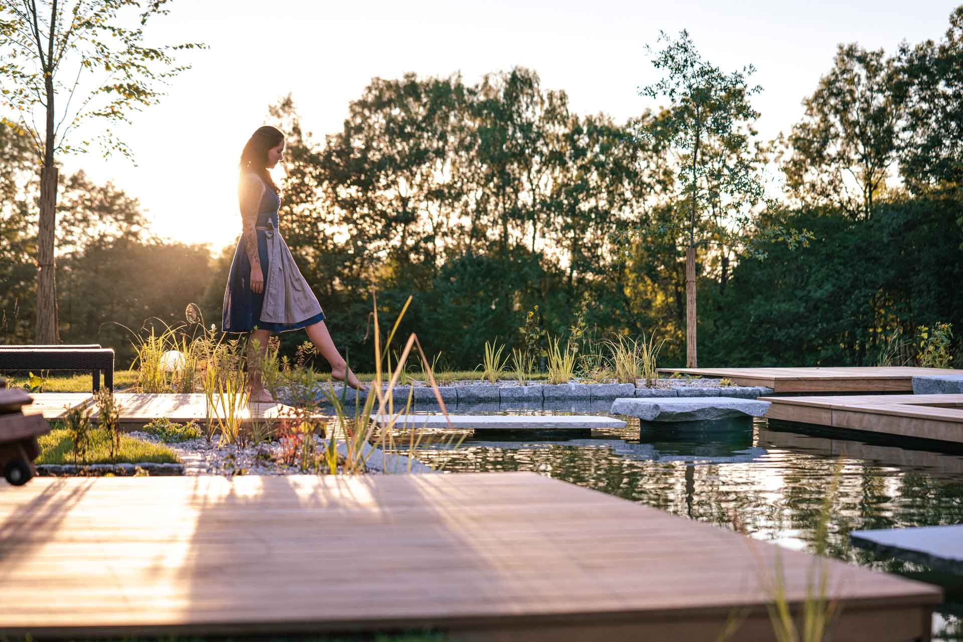 Frau im Dirndl läuft am Rand des Biotop-Swimmingpools entlang im Wellnesshotel Waldeck Bodenmais.