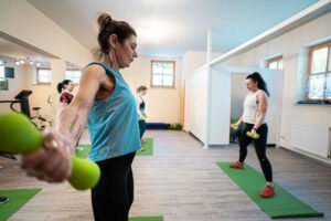 Mehrere Frauen nehmen an einem Fitnesskurs mit Gewichten im Wellnesshotel Waldeck Bodenmais teil, angeleitet von einer Trainerin.